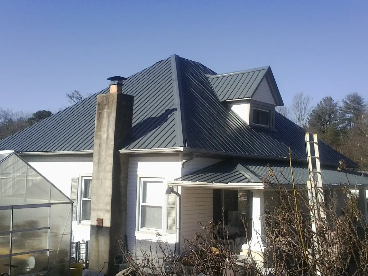 Dark blue standing seam metal roof on a white farmhouse with dormer — Slate & Tile Roof Repair by Roofing Brothers in East Northport