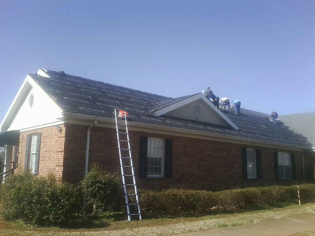 Crew tearing shingles off a brick ranch roof with a ladder set — Metal Roof Repair work by our crew in East Northport