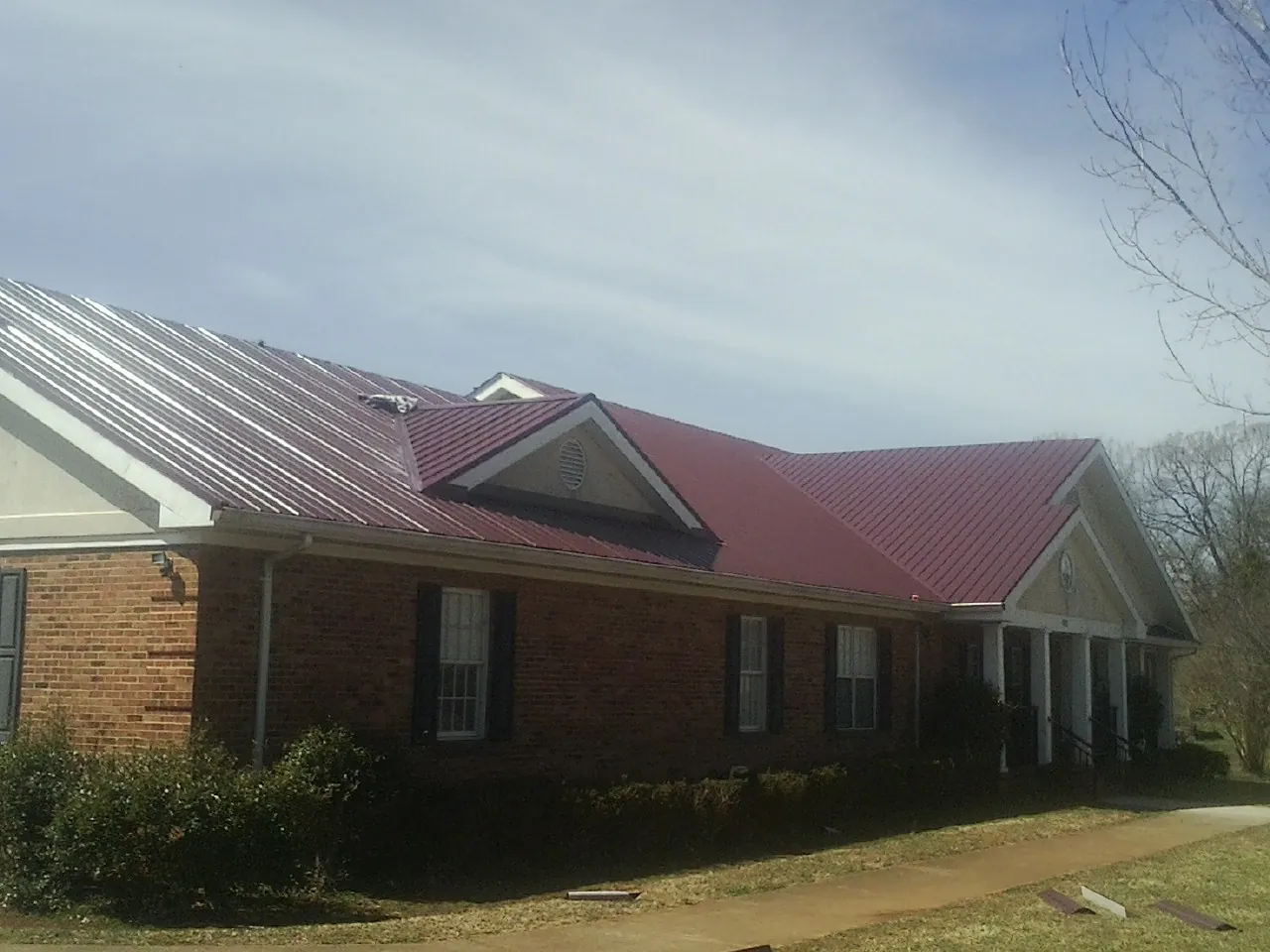 Red metal roof with gabled entries on a long brick building, from a Hail Damage Roof Repair job in East Northport