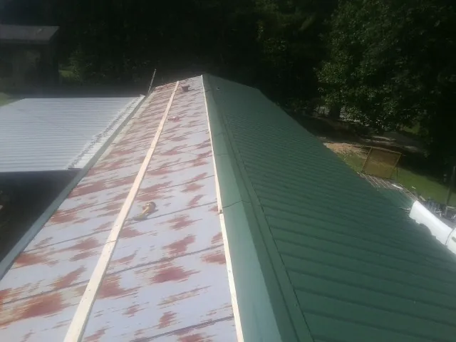 Old rusted panels beside newly installed green metal roofing — Wind Damage Roof Repair by Roofing Brothers in East Northport