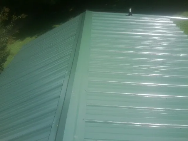 New green metal panels meeting at the ridge of a roof — Flat Roof Repair work by our crew in East Northport