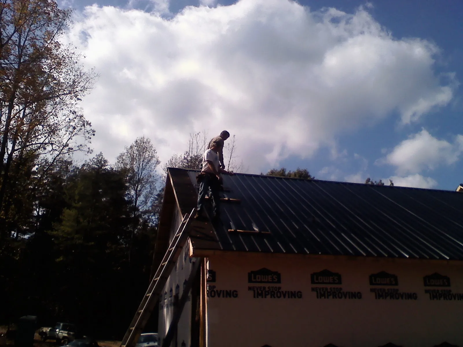 Roofer fastening dark metal panels high against a cloudy sky, from a Roof Inspection job in East Northport