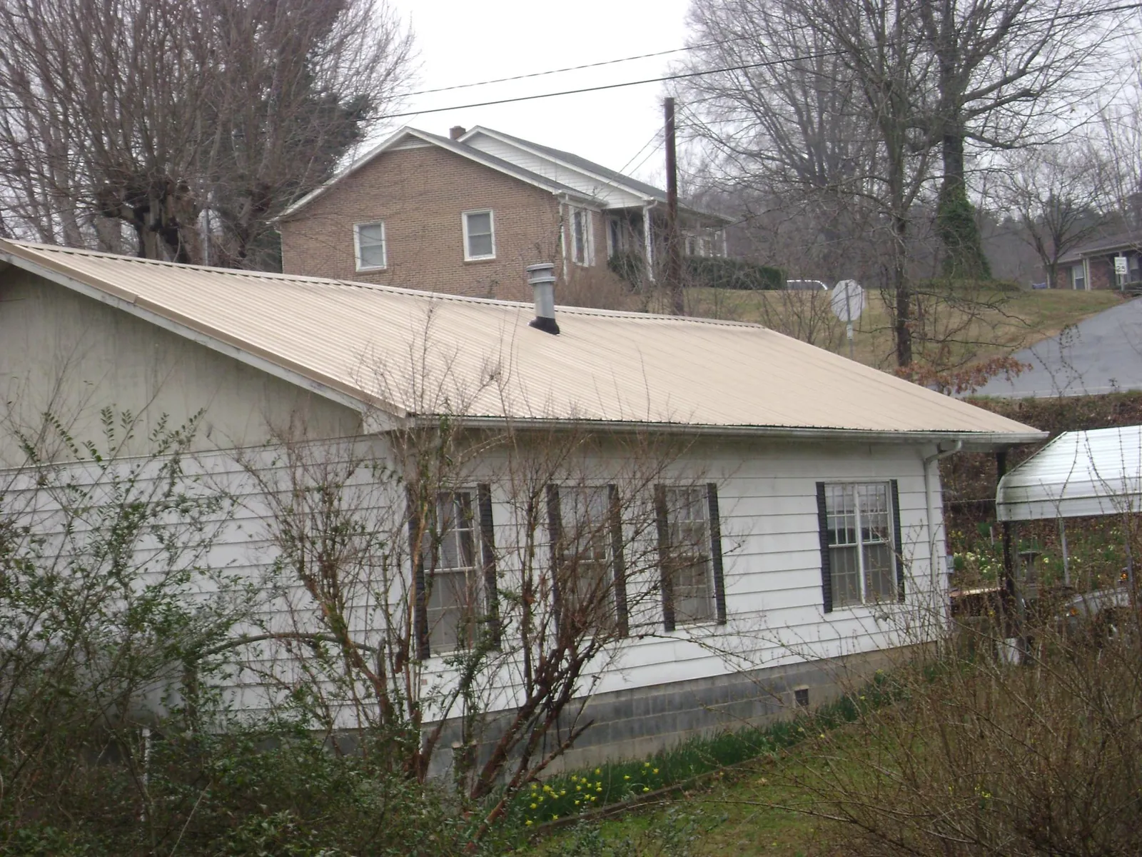 Tan metal roof on a white sided house set into a hillside — Commercial Roofing by Roofing Brothers in East Northport